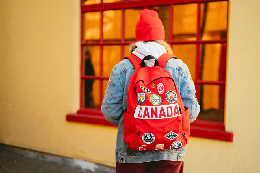 Person in a red beanie and denim jacket with a Northern Icons Canada Classic Backpack by a window.