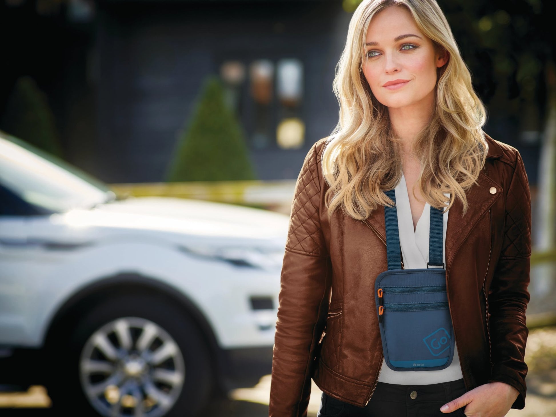 Woman in a brown leather jacket holds a Go Travel RFID Passport Pouch outdoors near a white SUV.