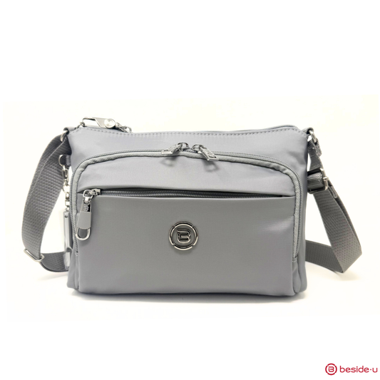 Product Image – The Beside-U Jubilee Crossbody is a gray bag with zip pockets, RFID pocket, adjustable strap, and logo emblem.