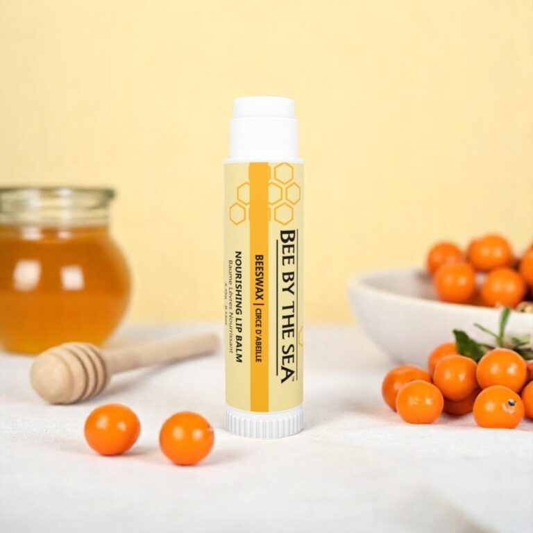 Bee by the Sea Lip Balm stands upright, with honey, a dipper, and sea buckthorn berries in the background.