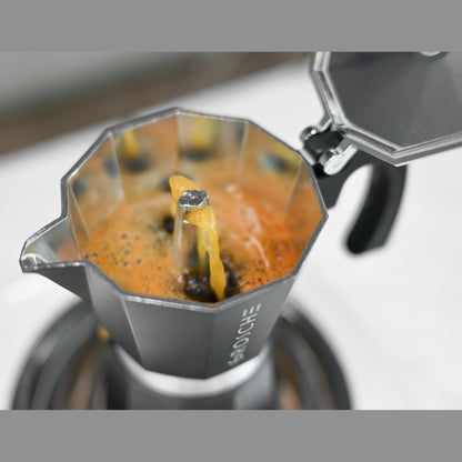 Close up of black moka pot brewing coffee with golden crema flowing from spout