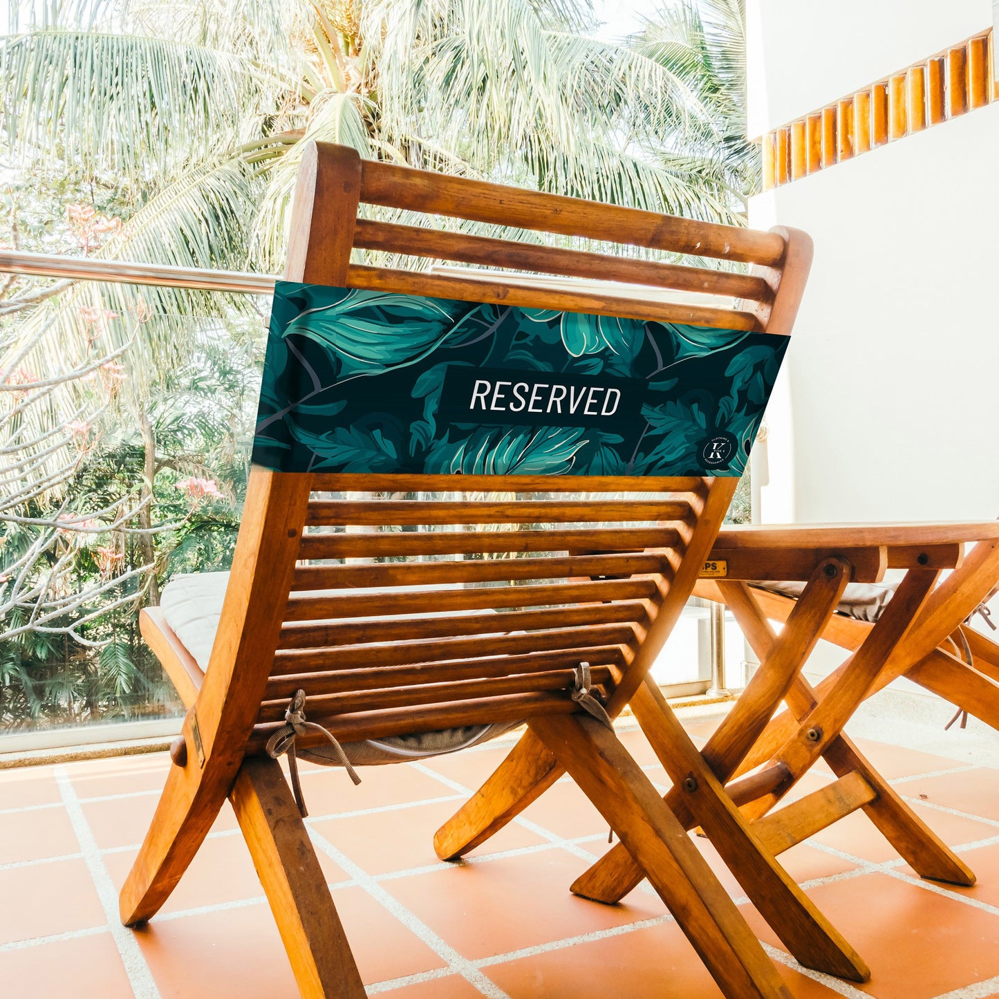 Lifestyle image of green foliage K5 Reserved Chair Sleeve, placed on a wooden balcony chair.