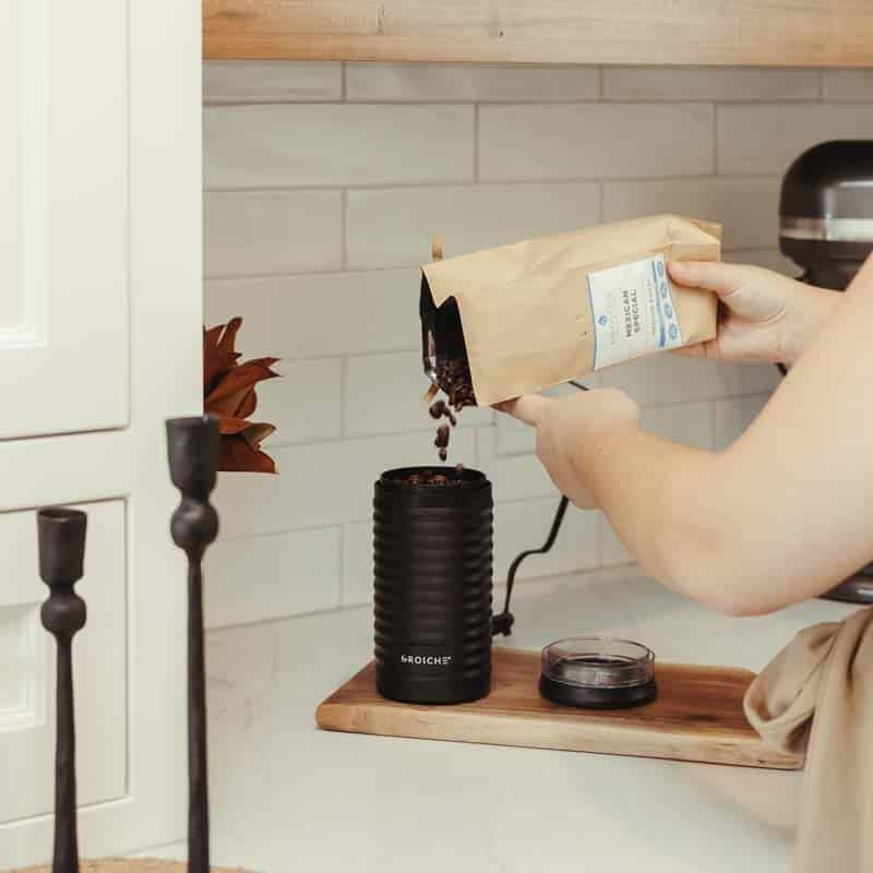 Pouring dark roasted coffee beans into open Grosche electric blade coffee grinder