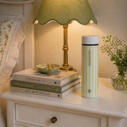 Green and white striped thermal bottle on nightstand beside books for home wellness