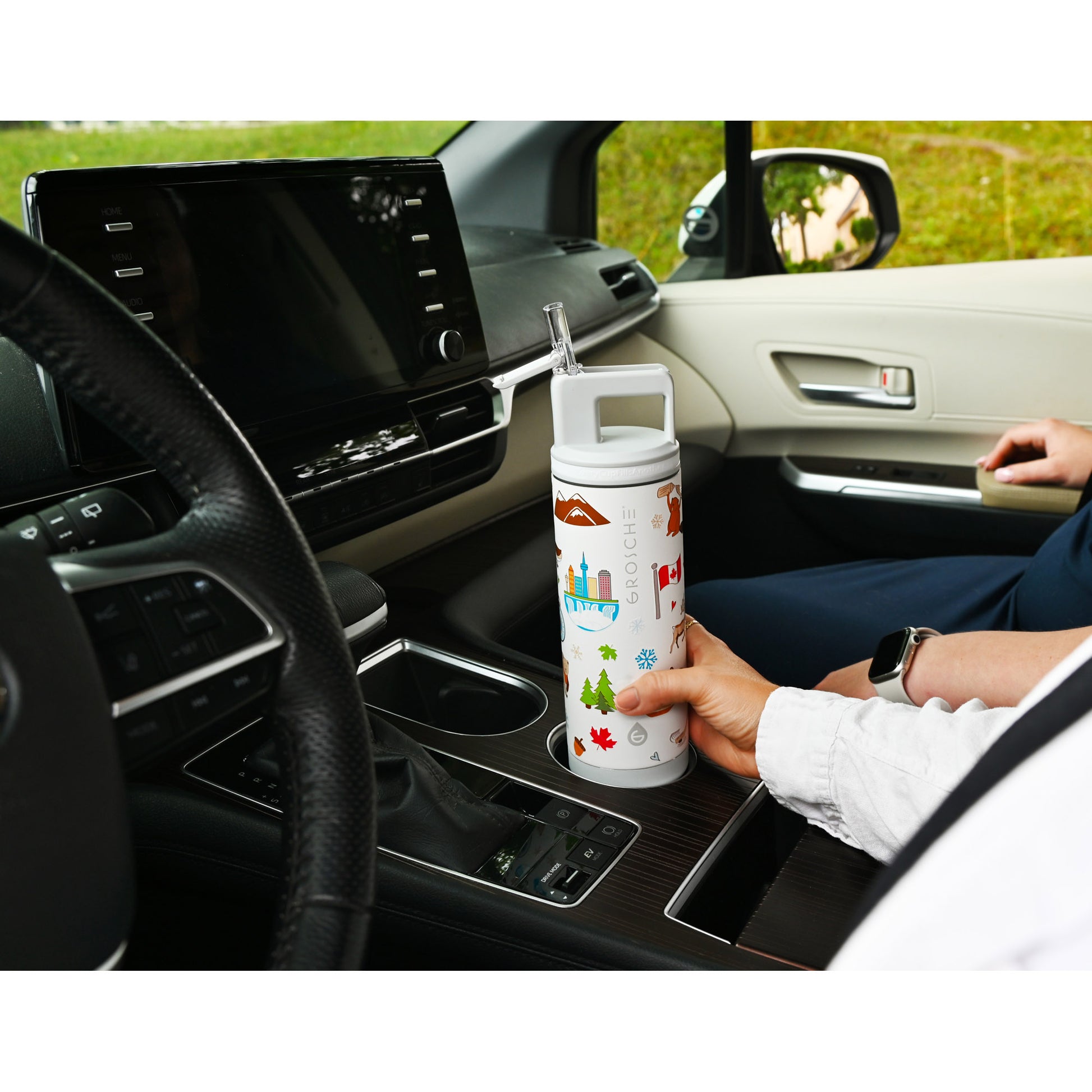Person in a car holds a Grosche Alpine 20oz Flip 'N Sip Insulated Water Bottle by the center console.