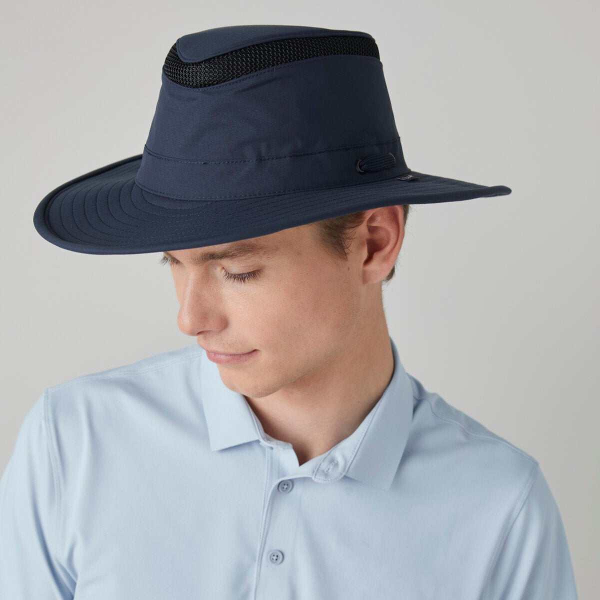Man wearing a light blue collared shirt and Tilley LTM6 Airflo® Hat for maximum sun coverage, looking down.