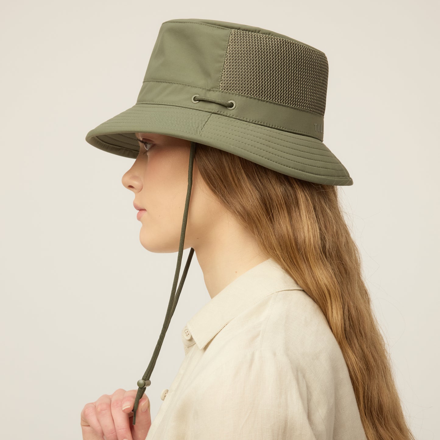 Person wearing a thyme green Tilley LTM1 Airflo® Bucket Hat with chin strap, side view.