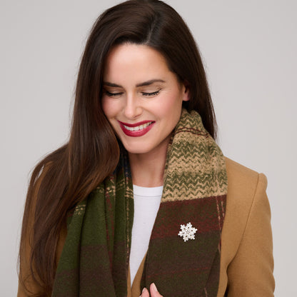 A woman wears a Howard’s Green Plaid Fringe Scarf - ONLINE ONLY with a silver snowflake-shaped brooch.