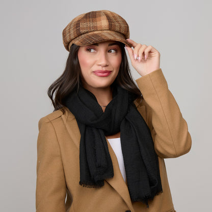 A woman wears a structured, brown Howard’s Tartan Plaid Newsboy Hat, a black scarf, and a tan coat.