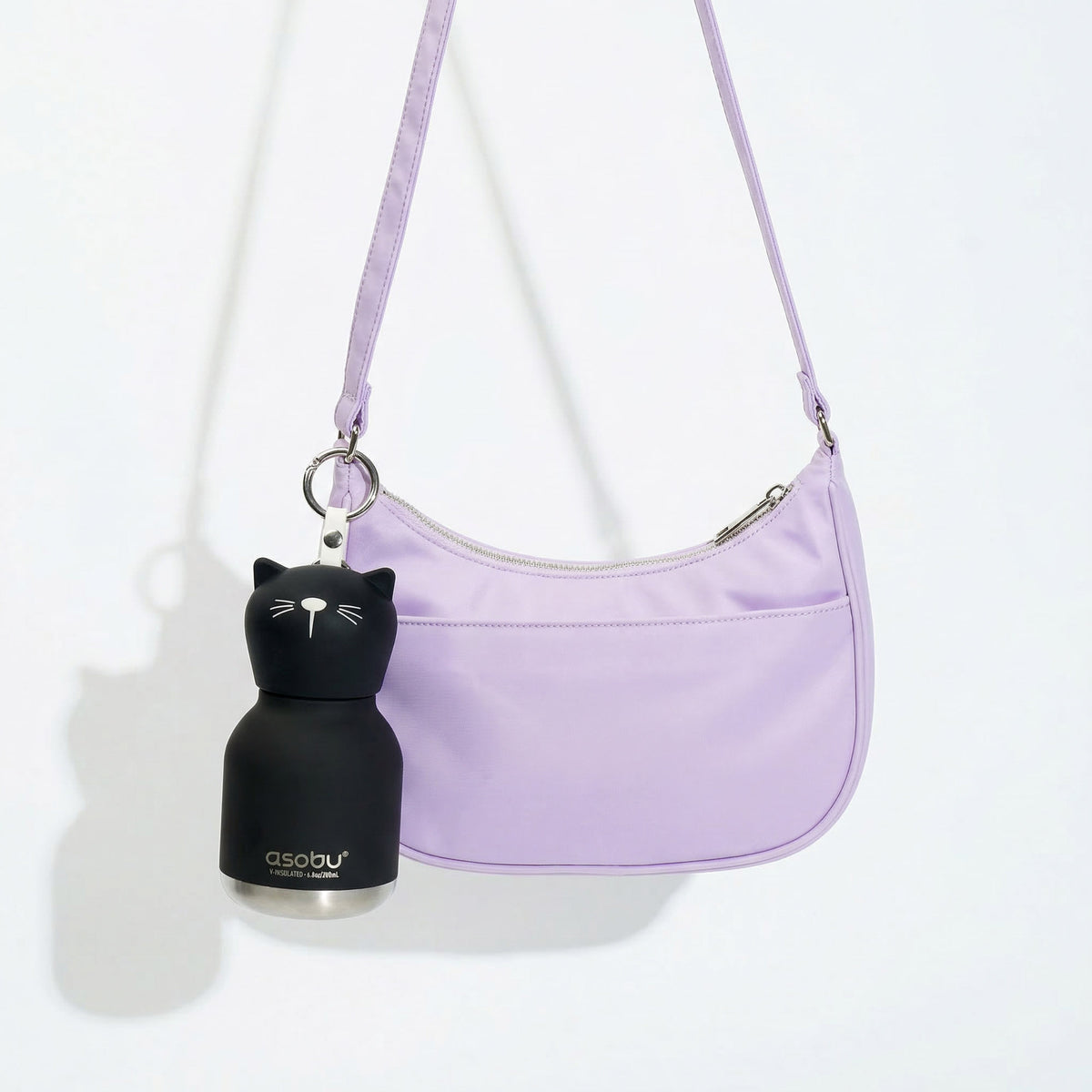 A black, cat-shaped Asobu Mini Bestie Bottle hanging from the strap of a light purple shoulder bag.