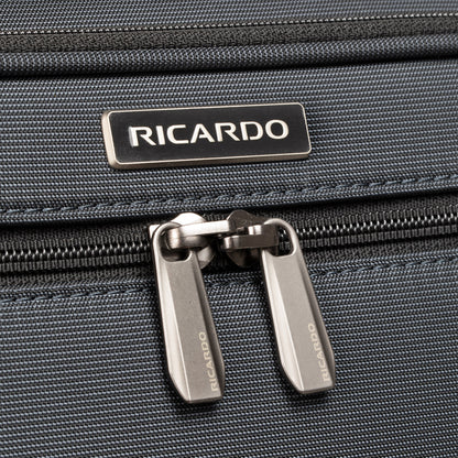 Close-up of Ricardo Beverly Hills Montecito 3.0 Large Check-In Spinner zipper and logo on dark grey fabric.
