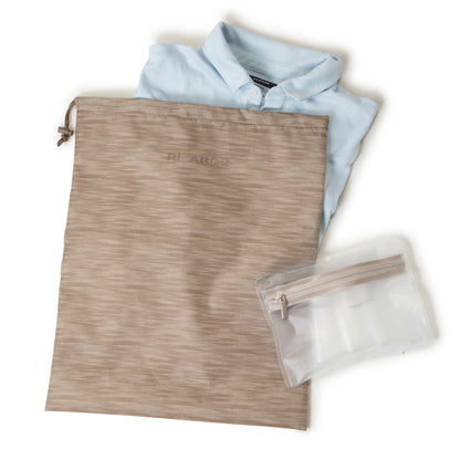 A folded light blue shirt, beige drawstring bag, and pouch beside Ricardo Beverly Hills Montecito 21" Carry-on.