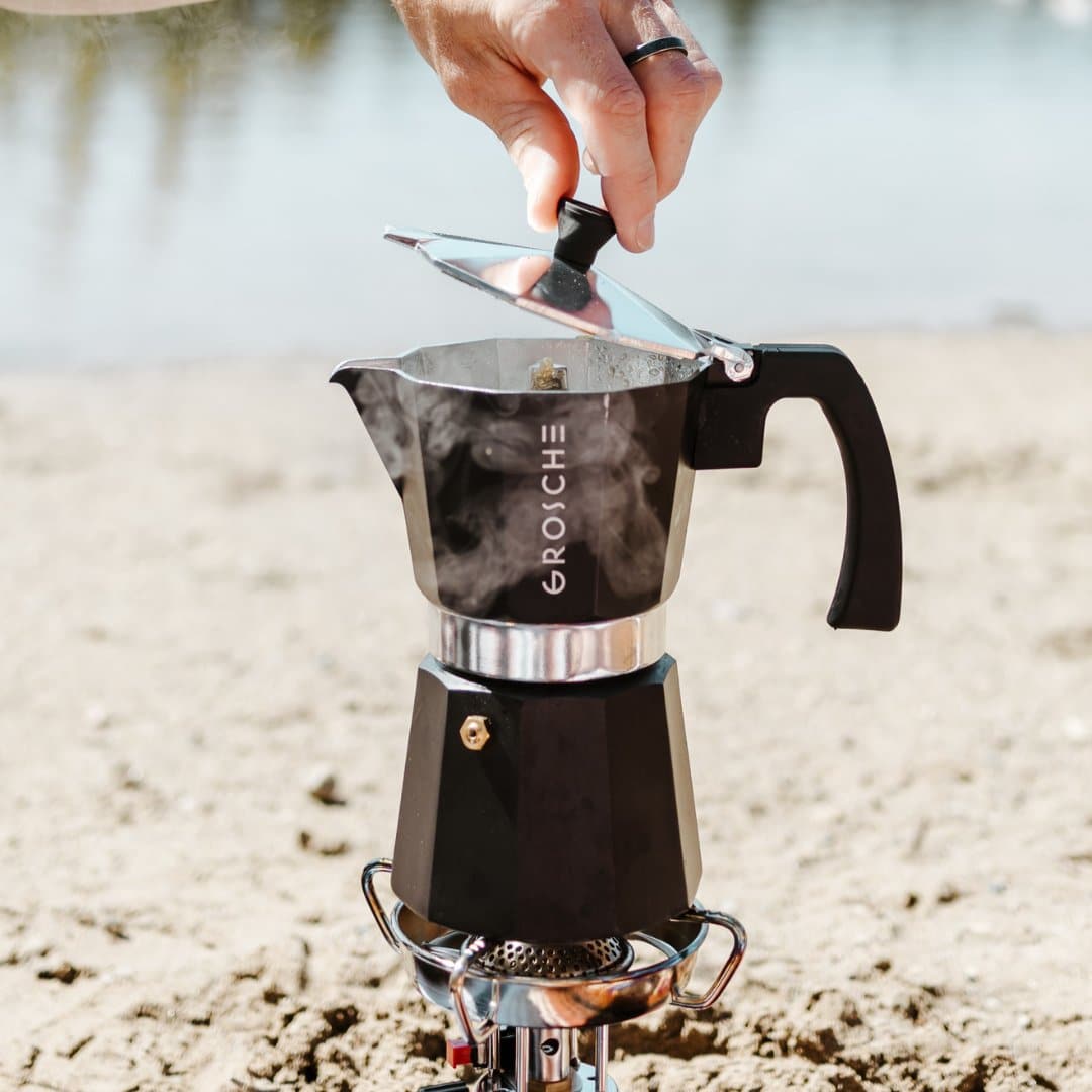 Black octagonal aluminum moka pot steaming on portable camping stove outdoors