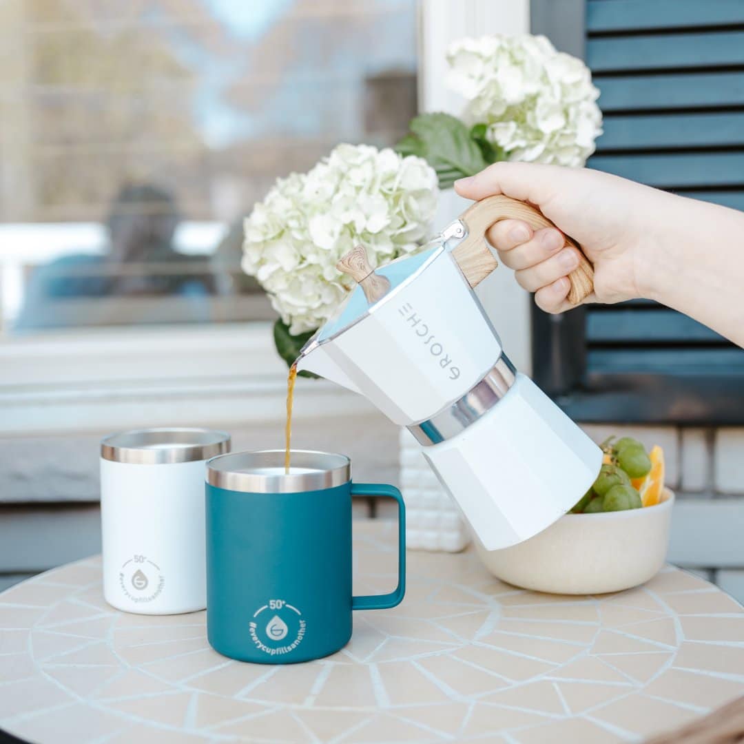 White moka pot pouring espresso into teal insulated tumbler on mosaic table