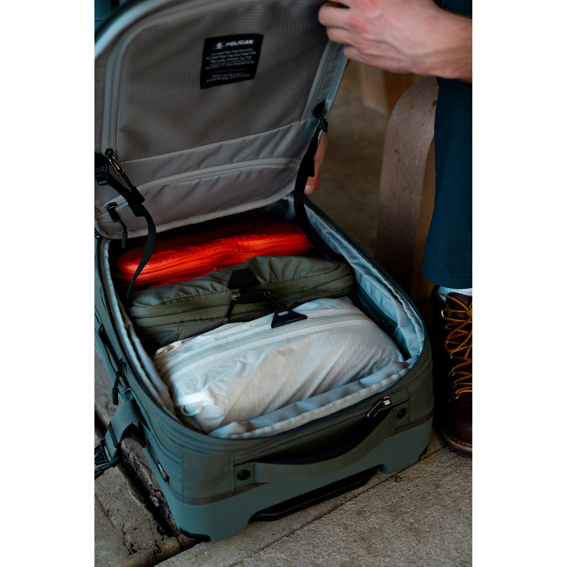 A person opens a Pelican™ Aegis Carry-on 4-Wheel Hybrid Duffel, revealing neatly organized clothes inside.