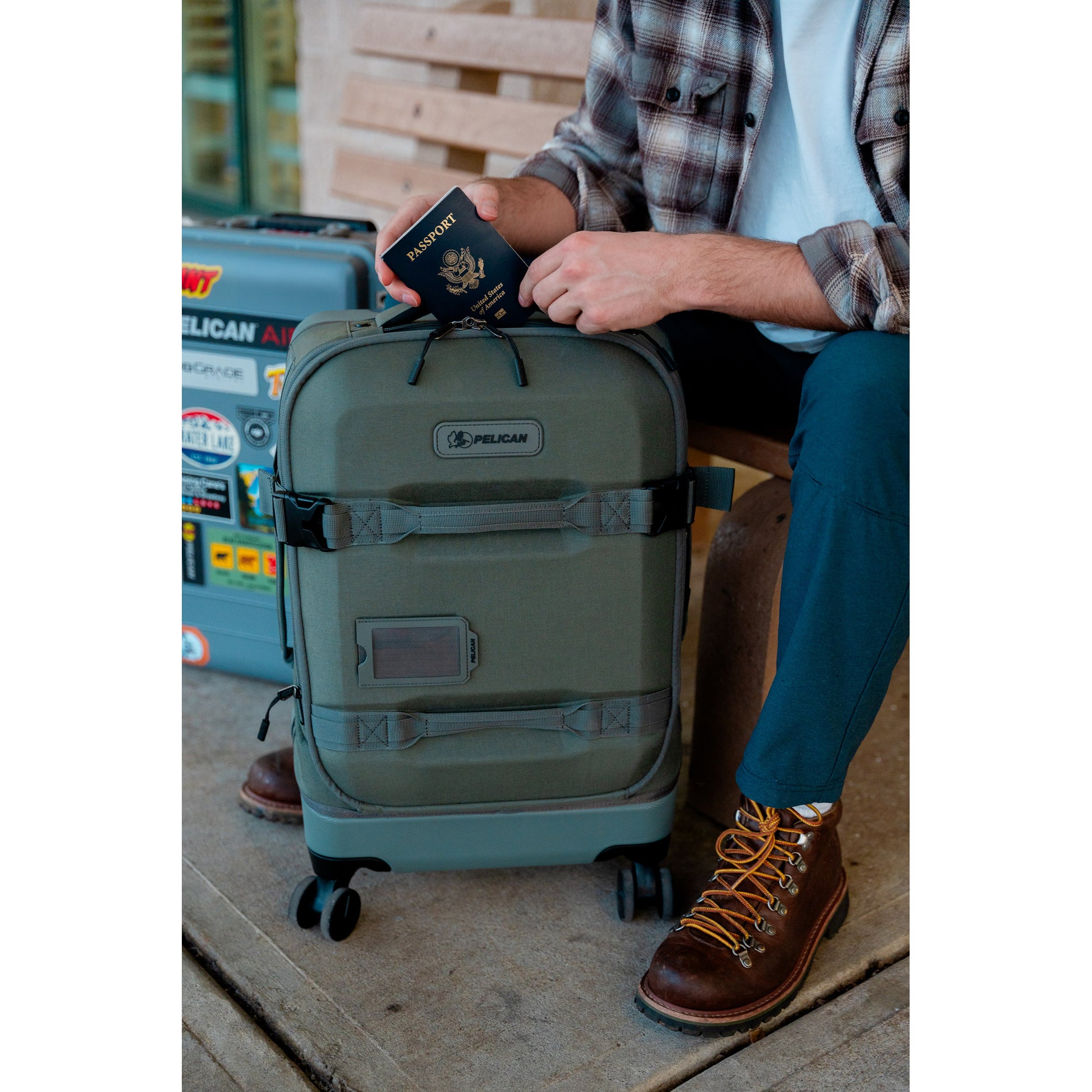 Person on bench with Pelican™ Aegis Carry-on 4-Wheel Hybrid Duffel, holding a passport and wearing brown boots.
