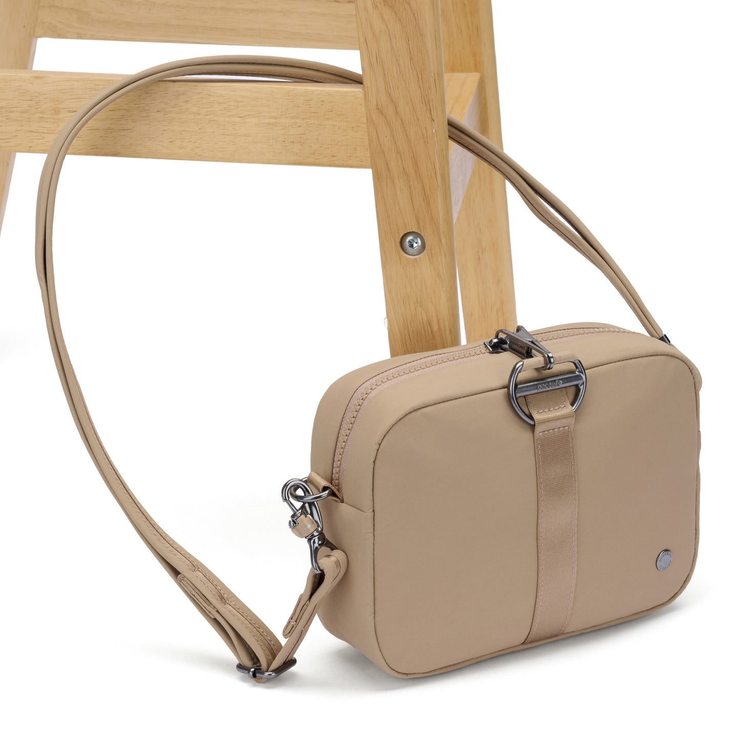 The Pacsafe® CX Anti-theft Square Crossbody in beige with RFIDsafe pockets sits on a wooden stool.
