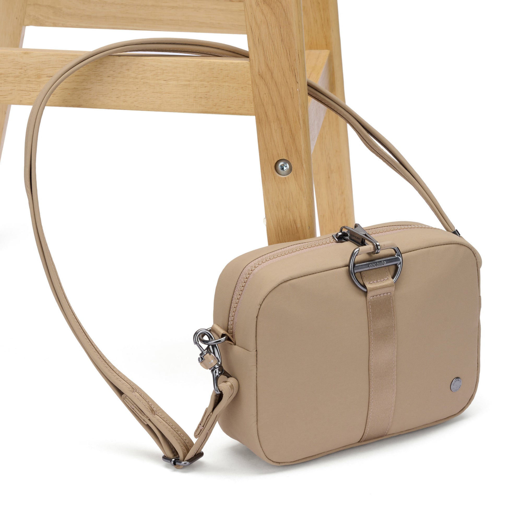 The Pacsafe® CX Anti-theft Square Crossbody in beige with RFIDsafe pockets sits on a wooden stool.