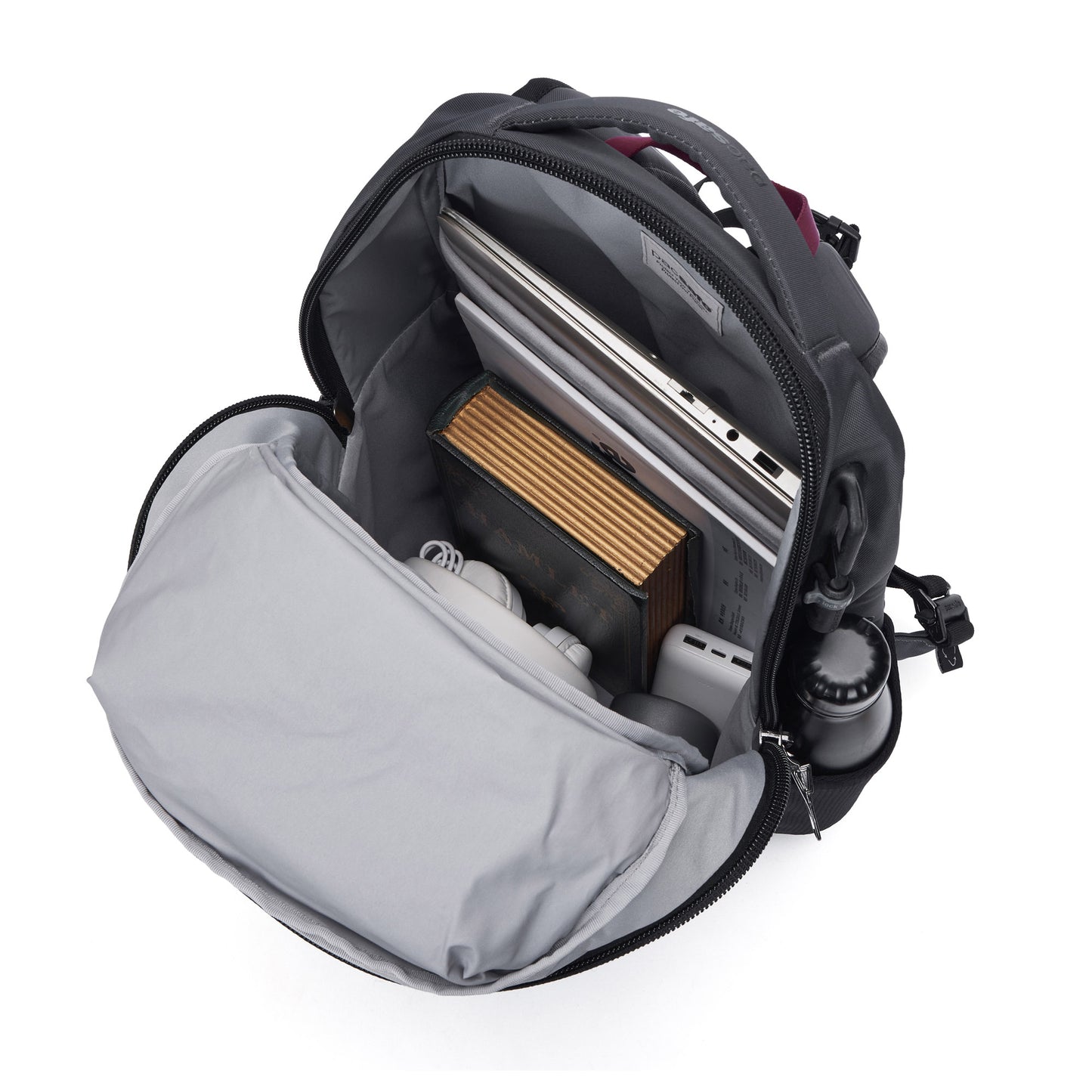 Pacsafe® EXP 28L Anti-Theft Backpack with laptop, book, headphones & bottle on white background.