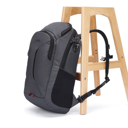 A Pacsafe® EXP 28L Anti-Theft Backpack by Pacsafe is strapped to a wooden stool with a loop around its leg.