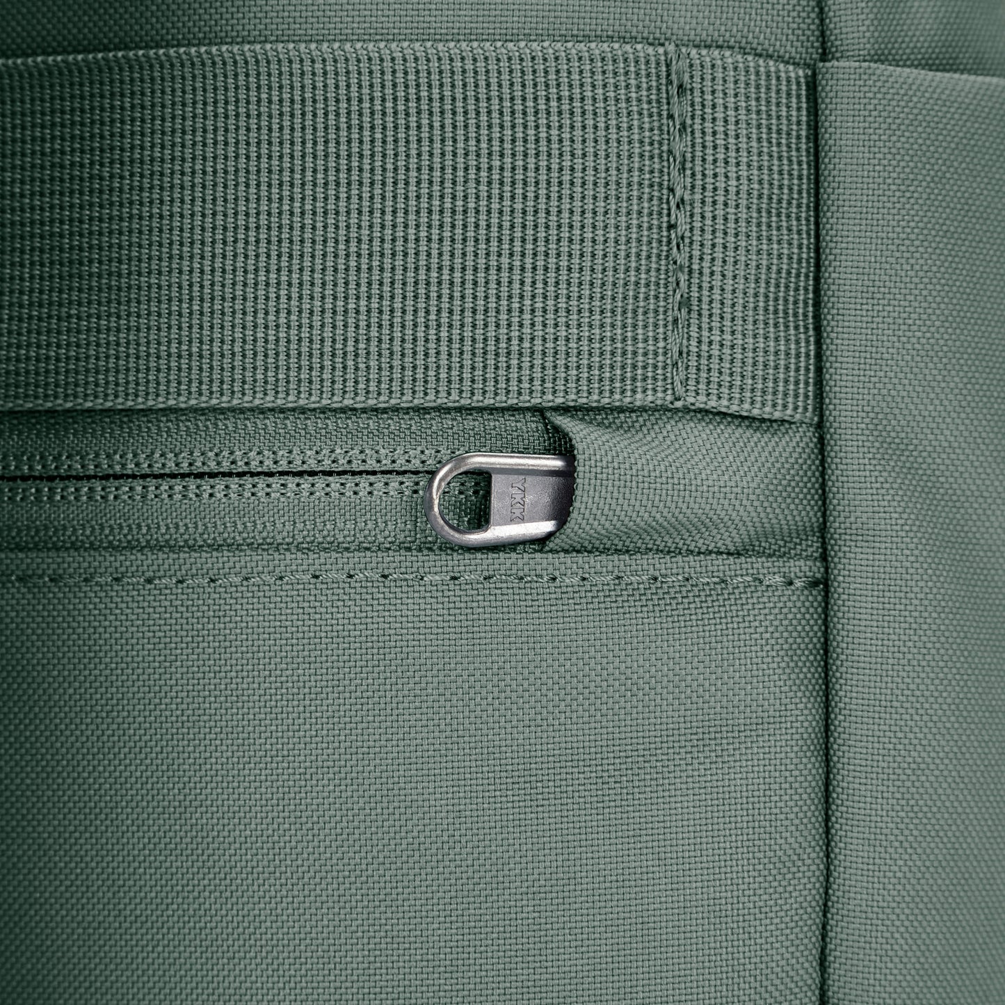 Close up of tucked zipper pull security feature on spruce green backpack