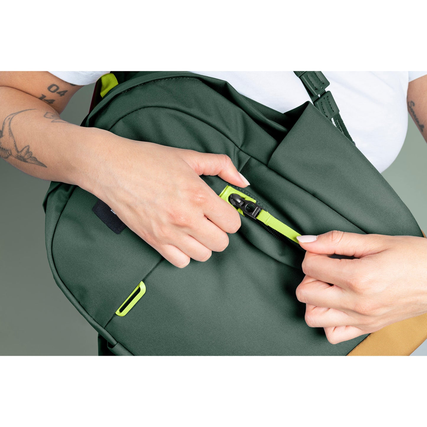 Person holding spruce green backpack opening security pocket on front of bag