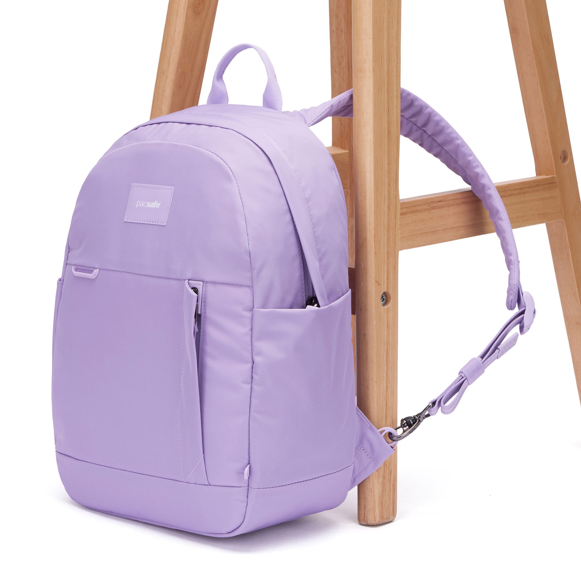 A Pacsafe® GO 15L Anti-theft Backpack in light purple is strapped securely to a wooden chair.