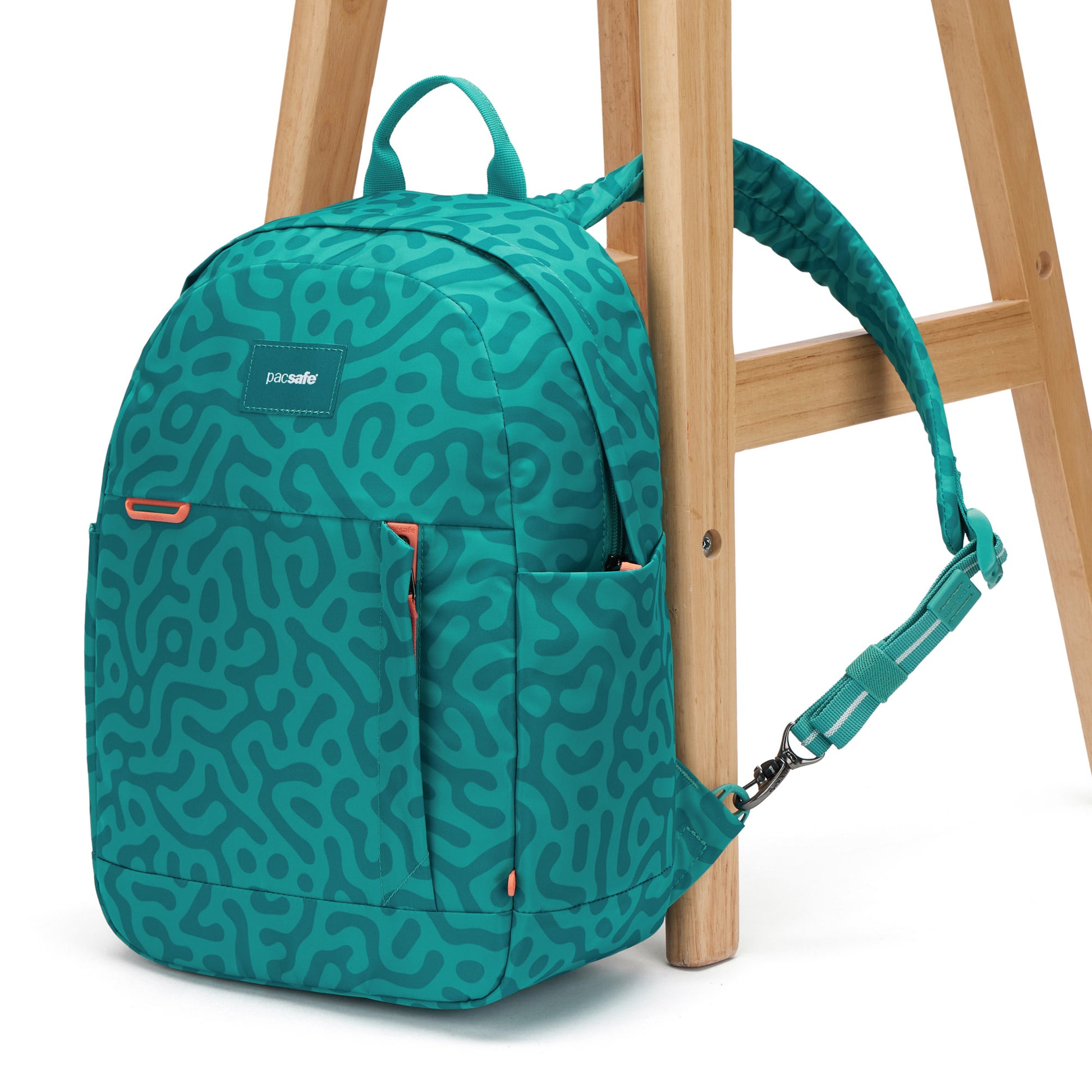 Pacsafe GO 15L backpack in reef green abstract print, with strap attached to a chair leg.