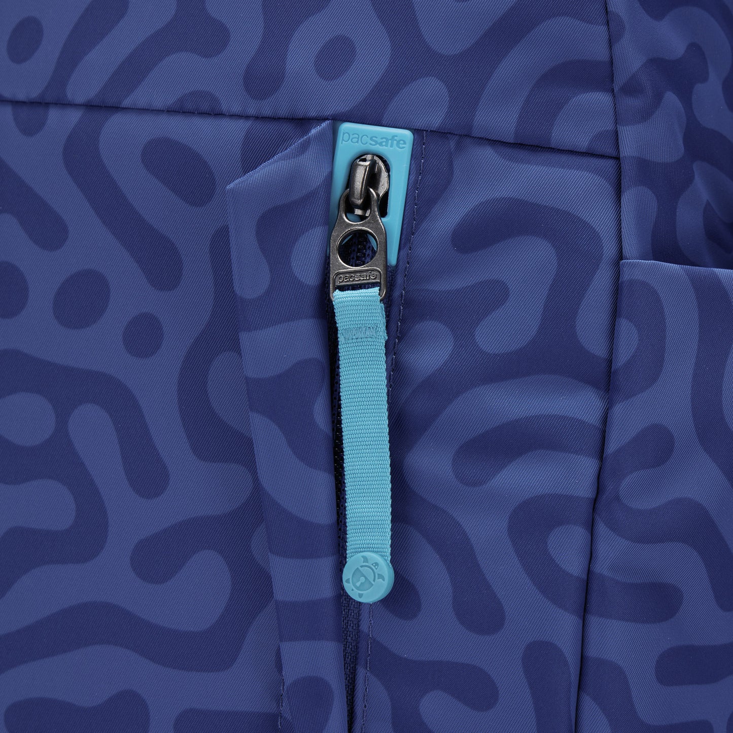 Close-up of turquoise zip pull on Pacsafe® GO 15L Anti-theft Backpack with patterned blue fabric.