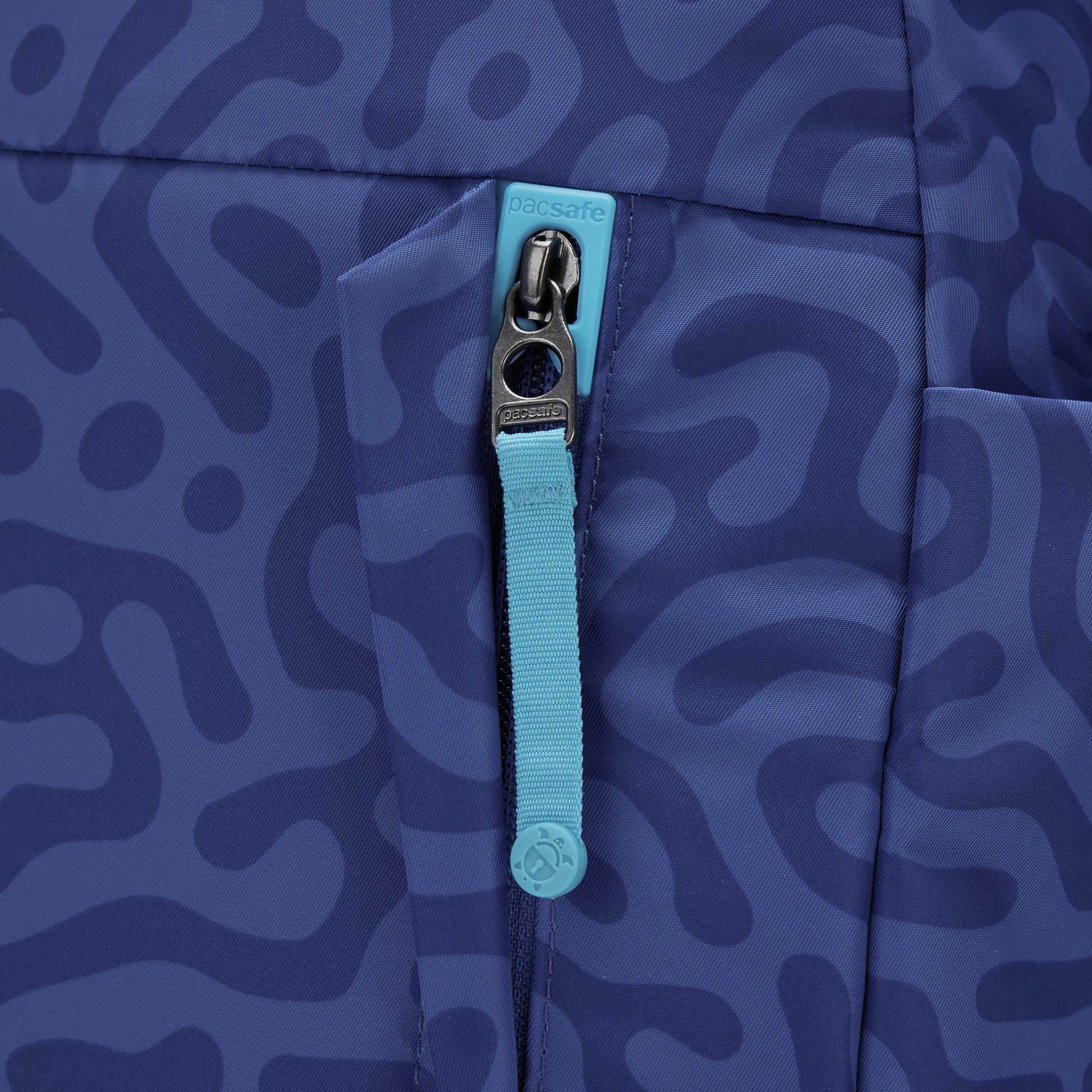 Close-up of turquoise zip pull on Pacsafe® GO 15L Anti-theft Backpack with patterned blue fabric.