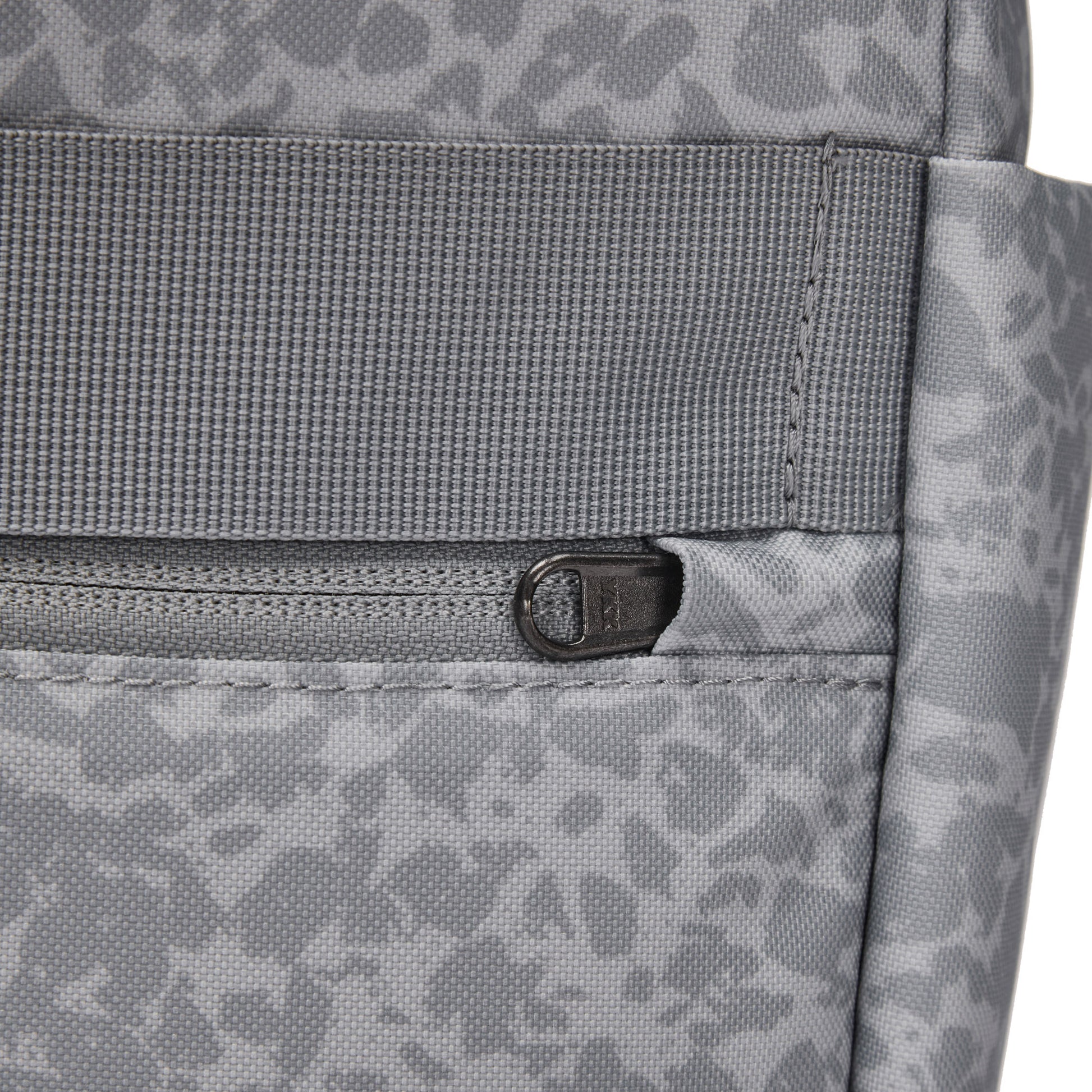 Close-up of Pacsafe® GO 15L Anti-theft Backpack in gray recycled polyester with front zipper and abstract pattern.