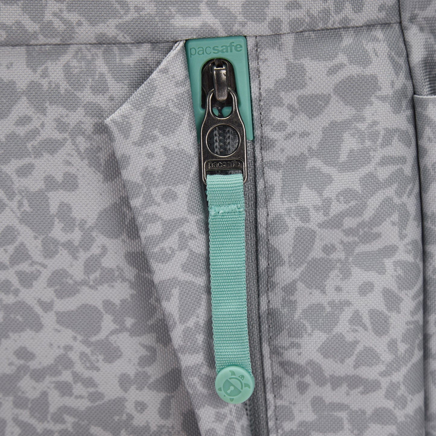 Close-up of a Pacsafe® GO 15L Anti-theft Backpack pocket with zipper and teal Pacsafe pull.