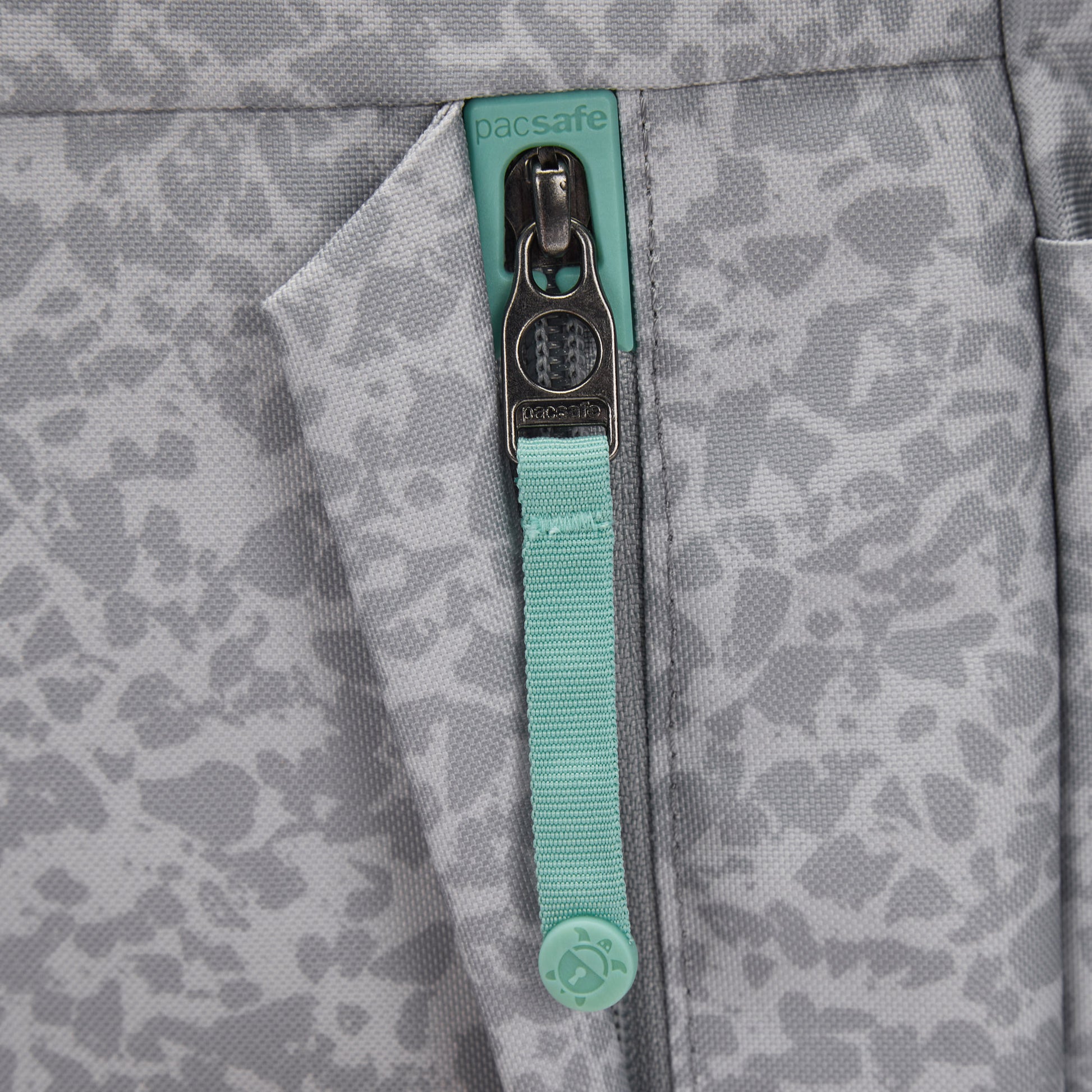 Close-up of a Pacsafe® GO 15L Anti-theft Backpack pocket with zipper and teal Pacsafe pull.