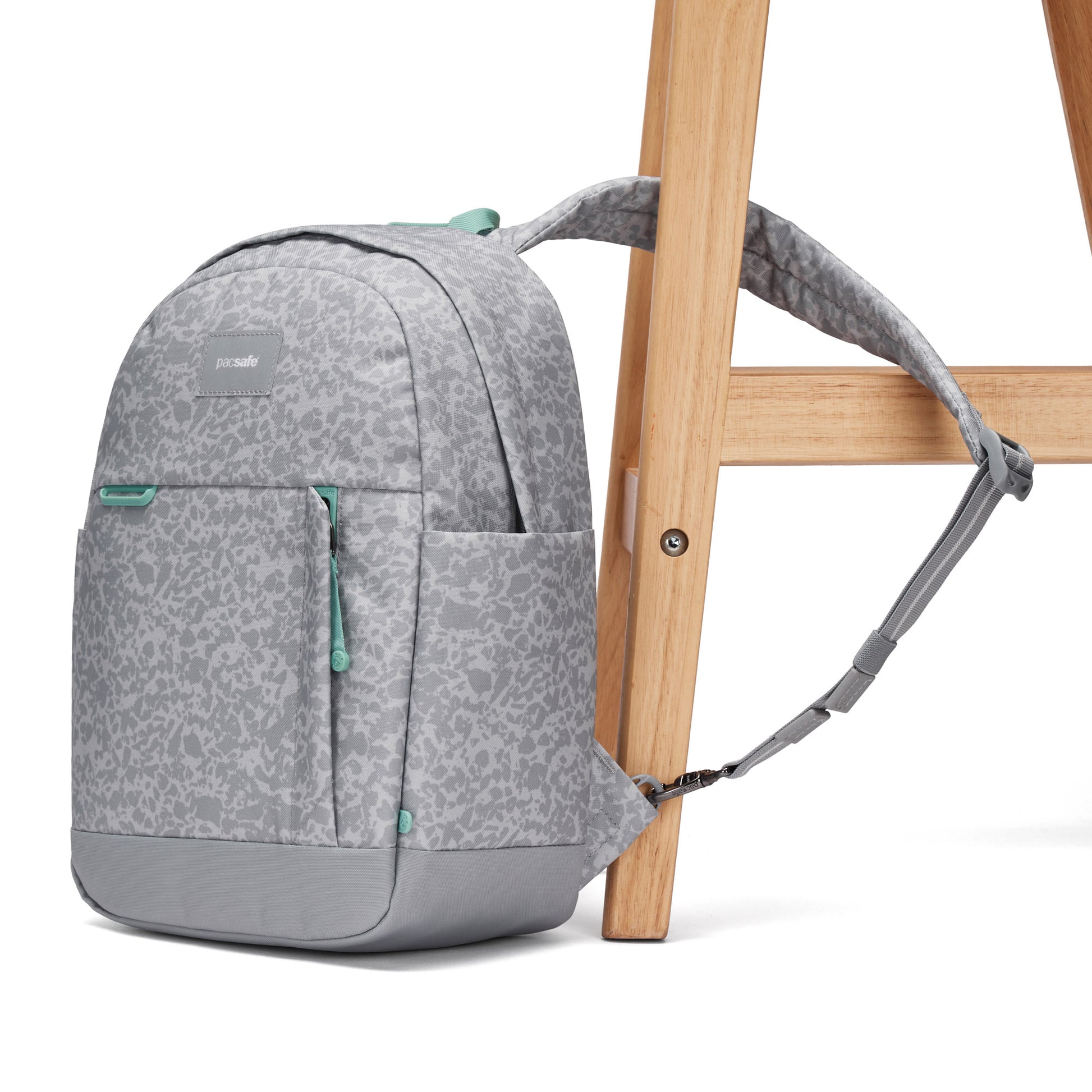 Pacsafe® GO 15L anti-theft backpack with teal zippers, RFID blocking, secured to a wooden chair leg.