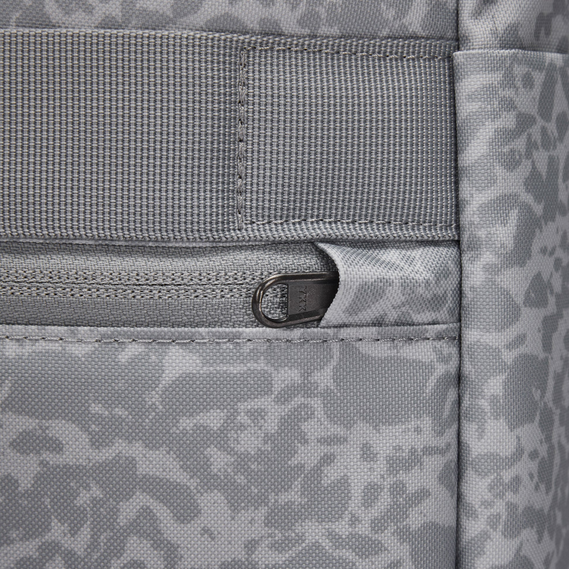 Close-up of Pacsafe® GO 25L Anti-theft Backpack in gray, with a zipper pocket and abstract pattern on fabric.