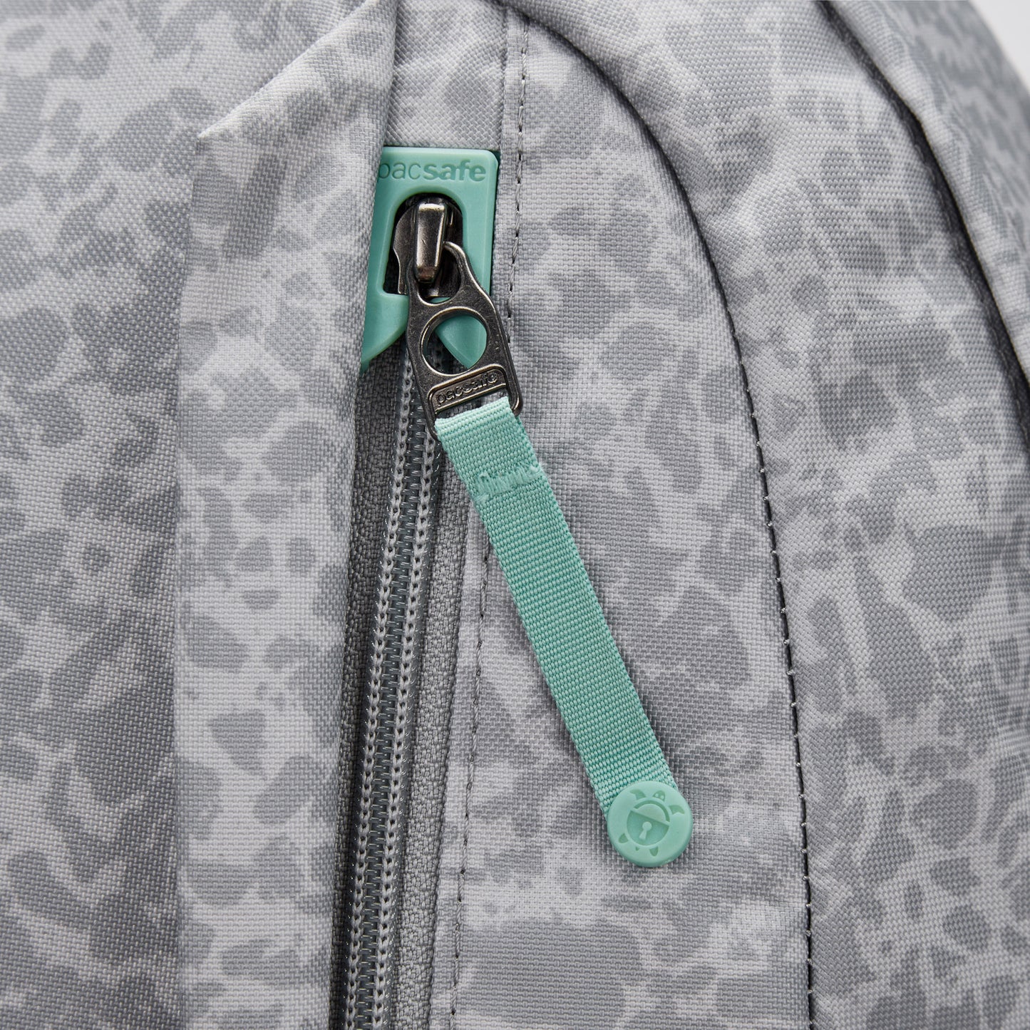 Close-up of a gray Pacsafe® GO 25L Anti-theft Backpack with mint green zipper pull and visible Pacsafe tag.