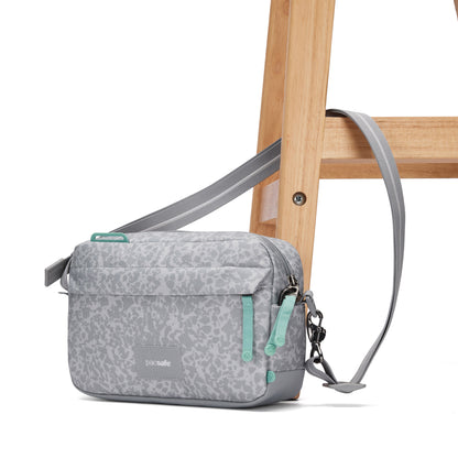 Pacsafe® GO Anti-Theft Crossbody Bag with green zippers on a stool against a white background.