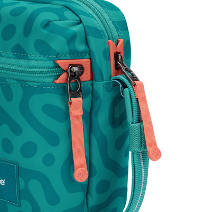 Close-up of Pacsafe® GO Anti-Theft Micro Crossbody in teal with wavy patterns, orange zippers, and teal strap.