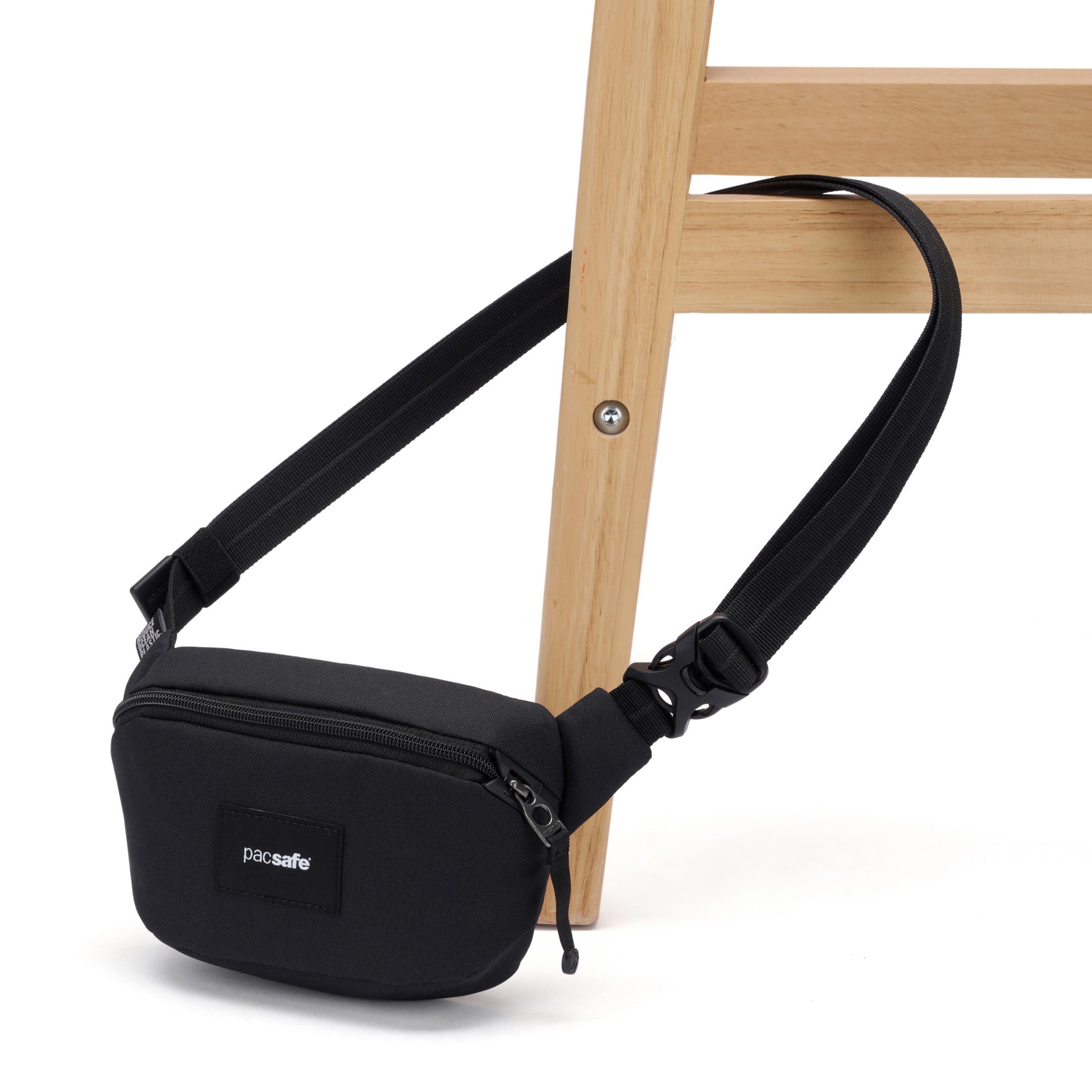 A black Pacsafe® GO Anti-Theft Micro Sling is secured around the leg of a light wooden chair.
