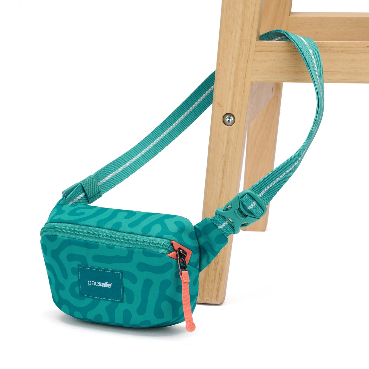 A teal Pacsafe® GO Anti-Theft Micro Sling with orange zipper, draped over a wooden chair leg.