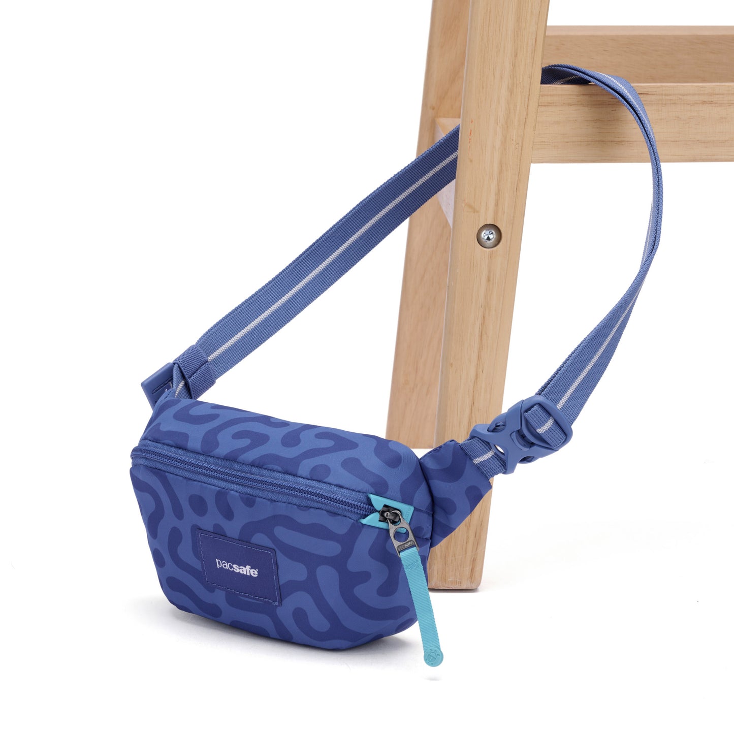Pacsafe® GO Anti-Theft Micro Sling in blue pattern with turquoise zipper, by Pacsafe, on a wooden chair leg.