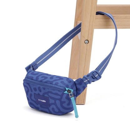 Pacsafe® GO Anti-Theft Micro Sling in blue pattern with turquoise zipper, by Pacsafe, on a wooden chair leg.