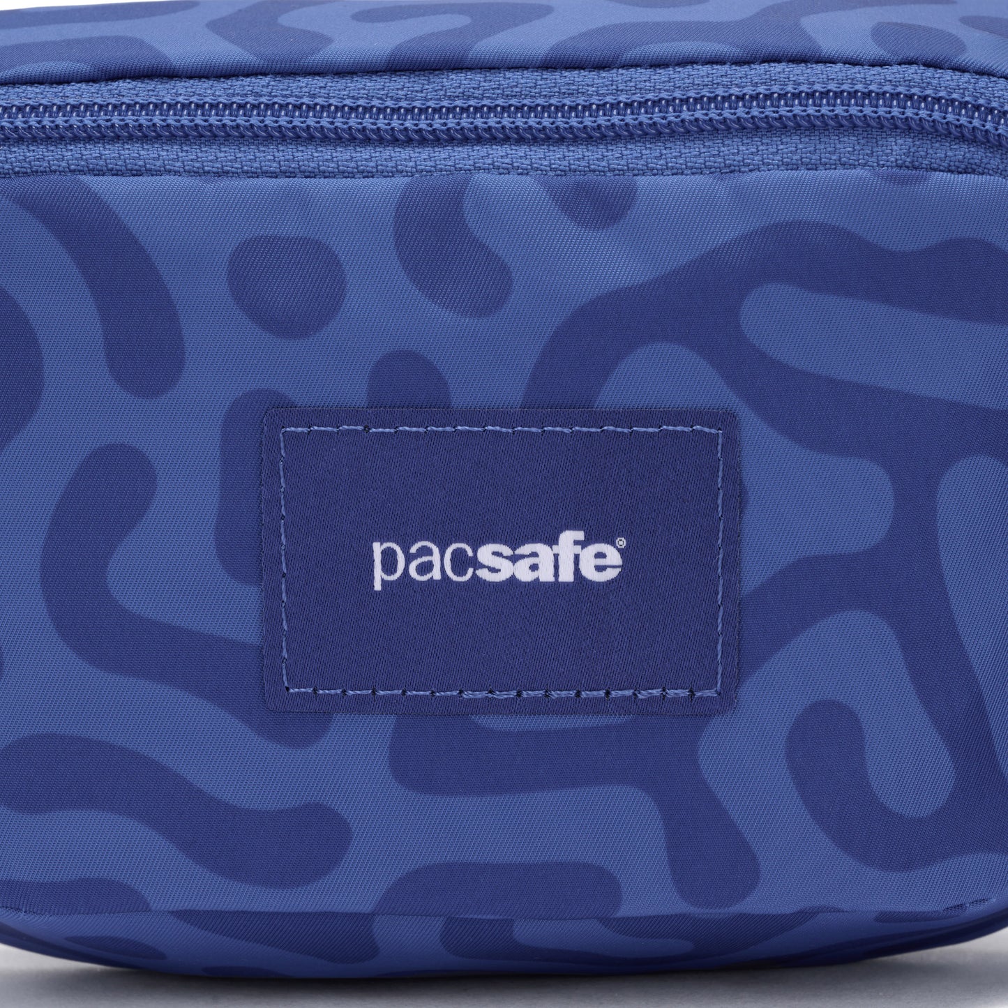 Close-up of the blue Pacsafe® GO Anti-Theft Micro Sling with abstract pattern, recycled polyester, and logo patch.