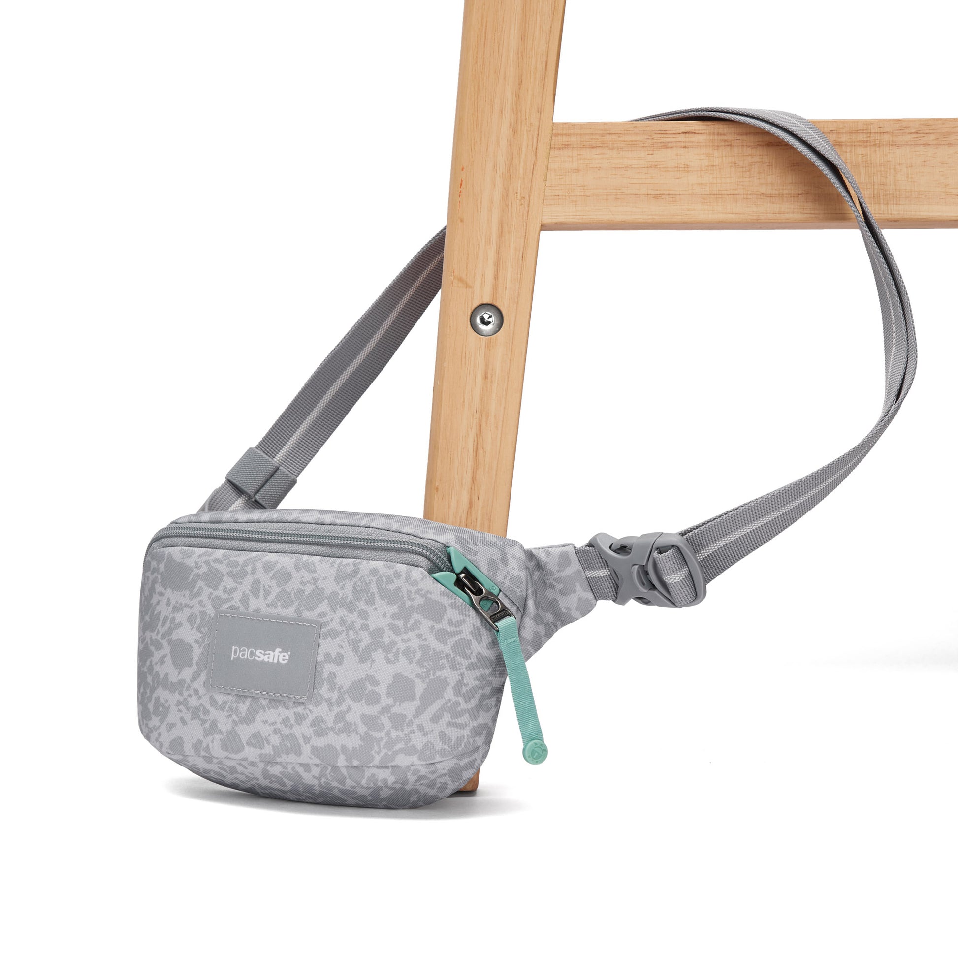 Pacsafe® GO Anti-Theft Micro Sling in gray, draped over a light wooden chair leg. Brand: Pacsafe.