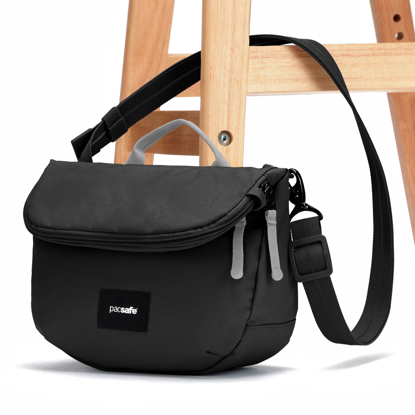 A small black Pacsafe® GO Anti-Theft Saddle Crossbody hangs on a wooden stool.
