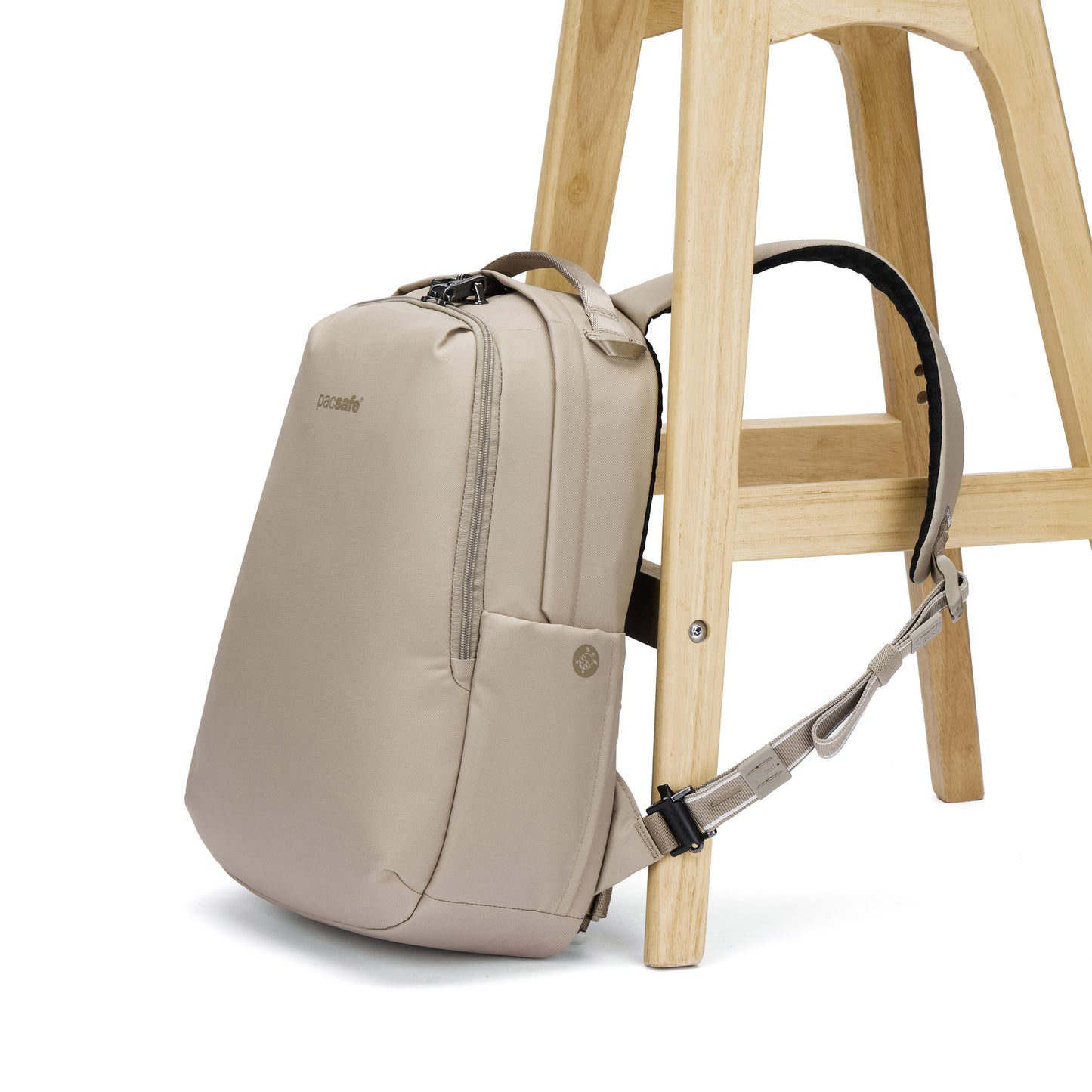 A Pacsafe® V 16L Anti-theft All-Around Backpack in beige leans on a stool, strap hanging over the leg.