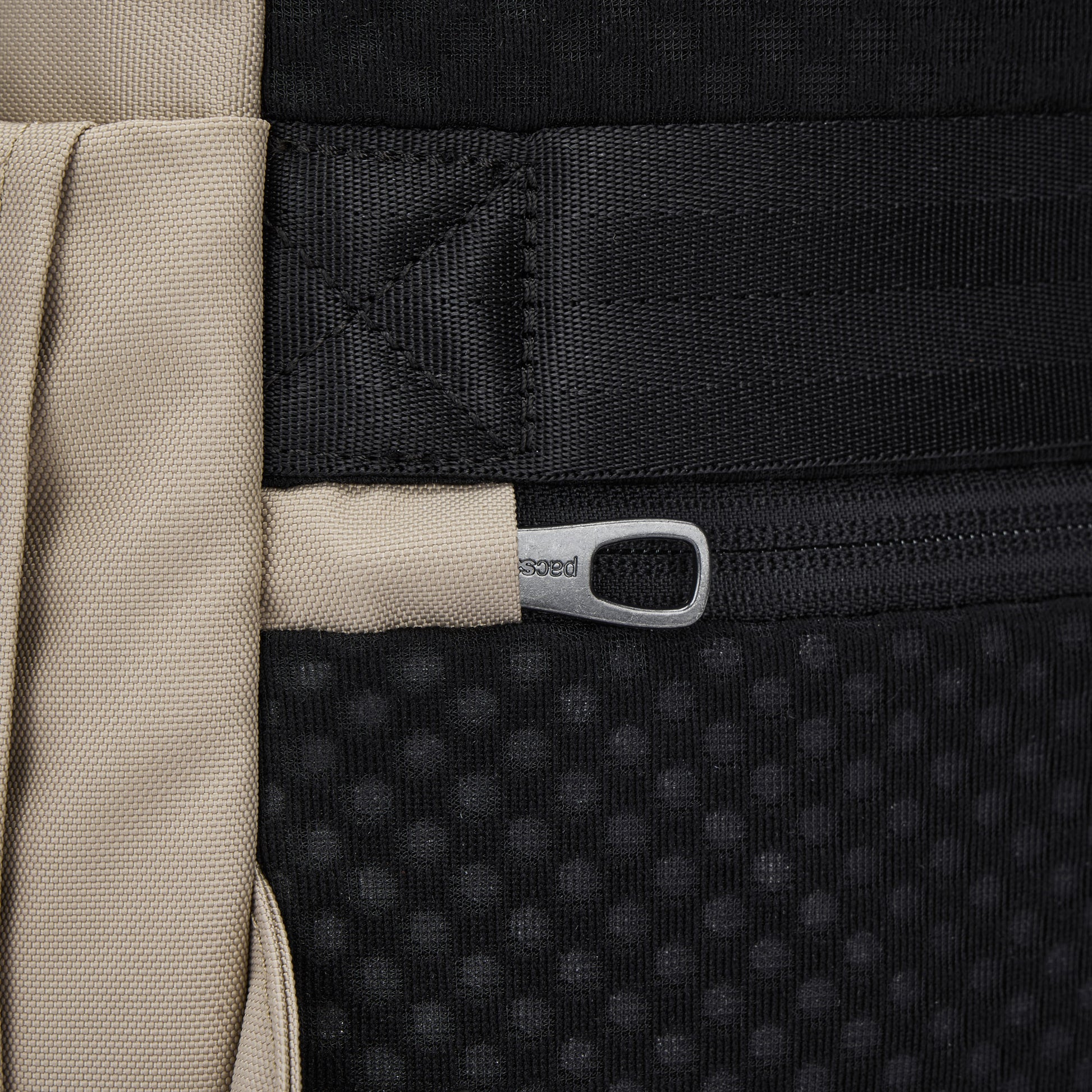 Close-up of beige strap and zipper on Pacsafe® V 16L Anti-theft All-Around Backpack in textured black.