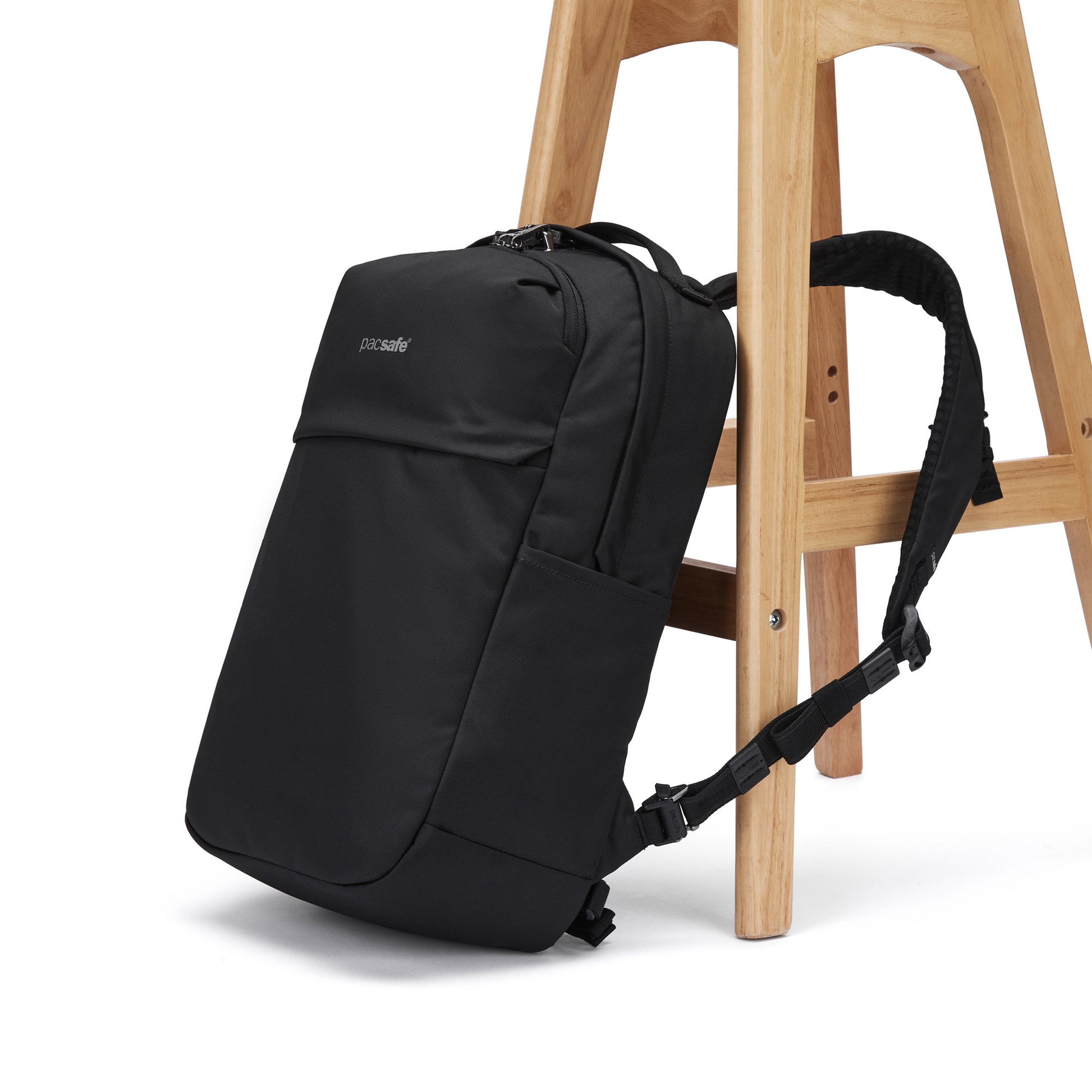 The Pacsafe® V 20L Anti-theft City Backpack by Pacsafe rests against a wooden stool on a white background.