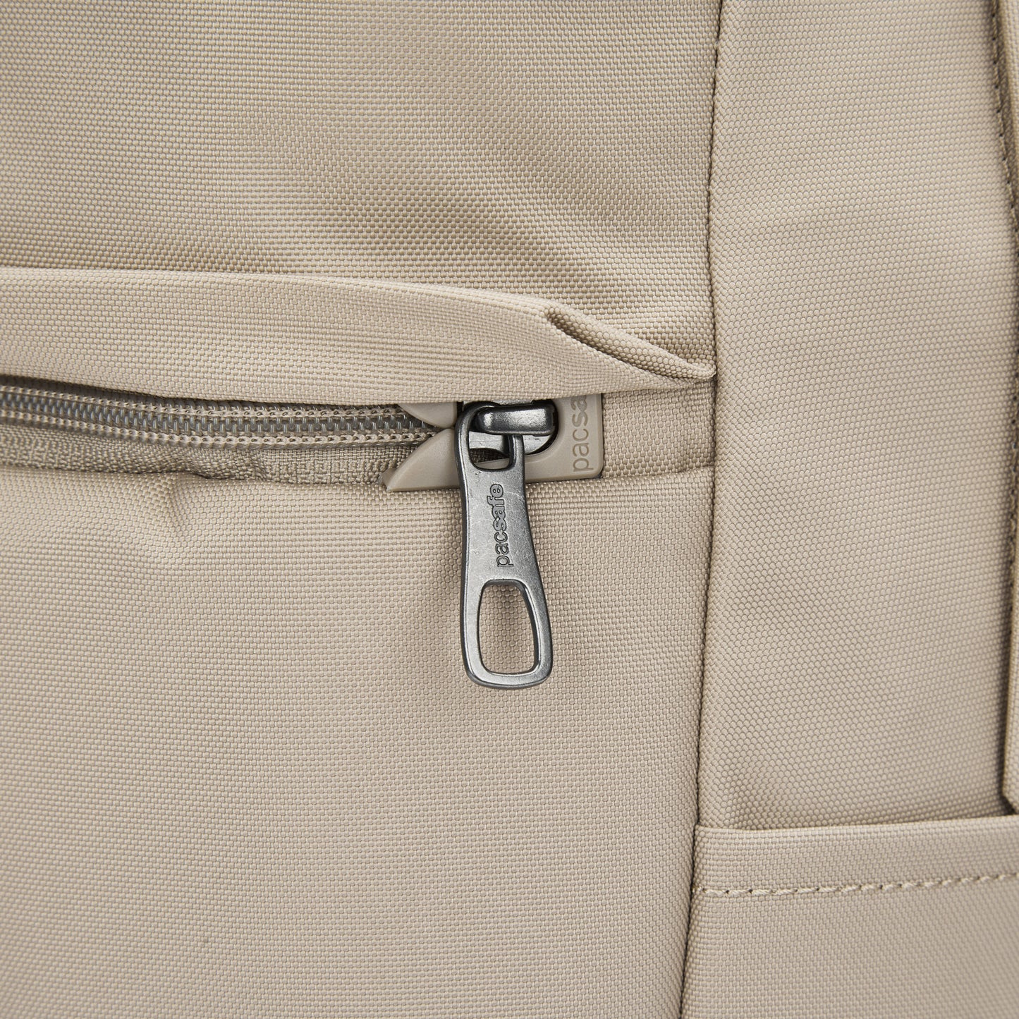 Close-up of Pacsafe® V 20L Anti-theft City Backpack pocket in beige with silver zipper, recycled polyester.