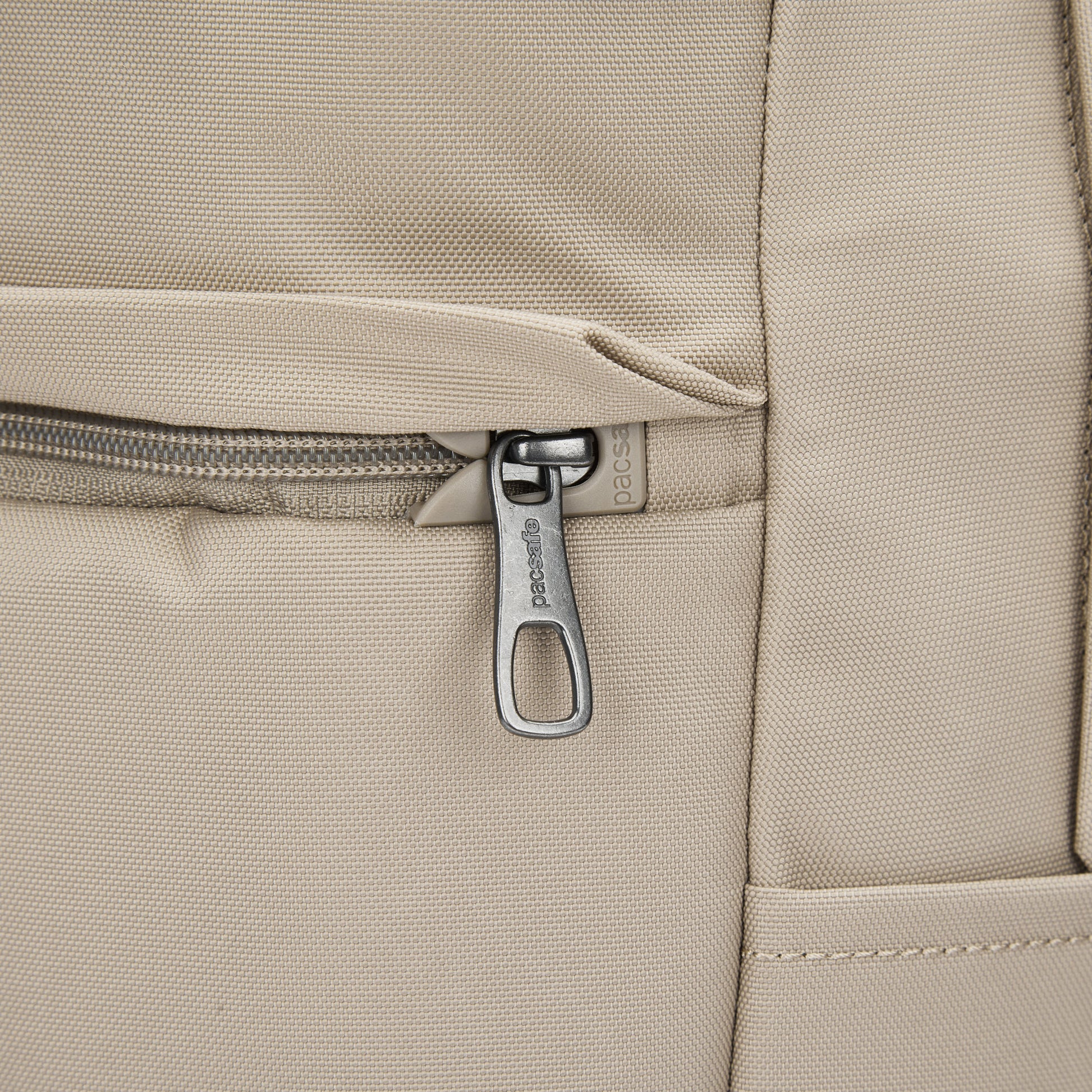 Close-up of Pacsafe® V 20L Anti-theft City Backpack pocket in beige with silver zipper, recycled polyester.